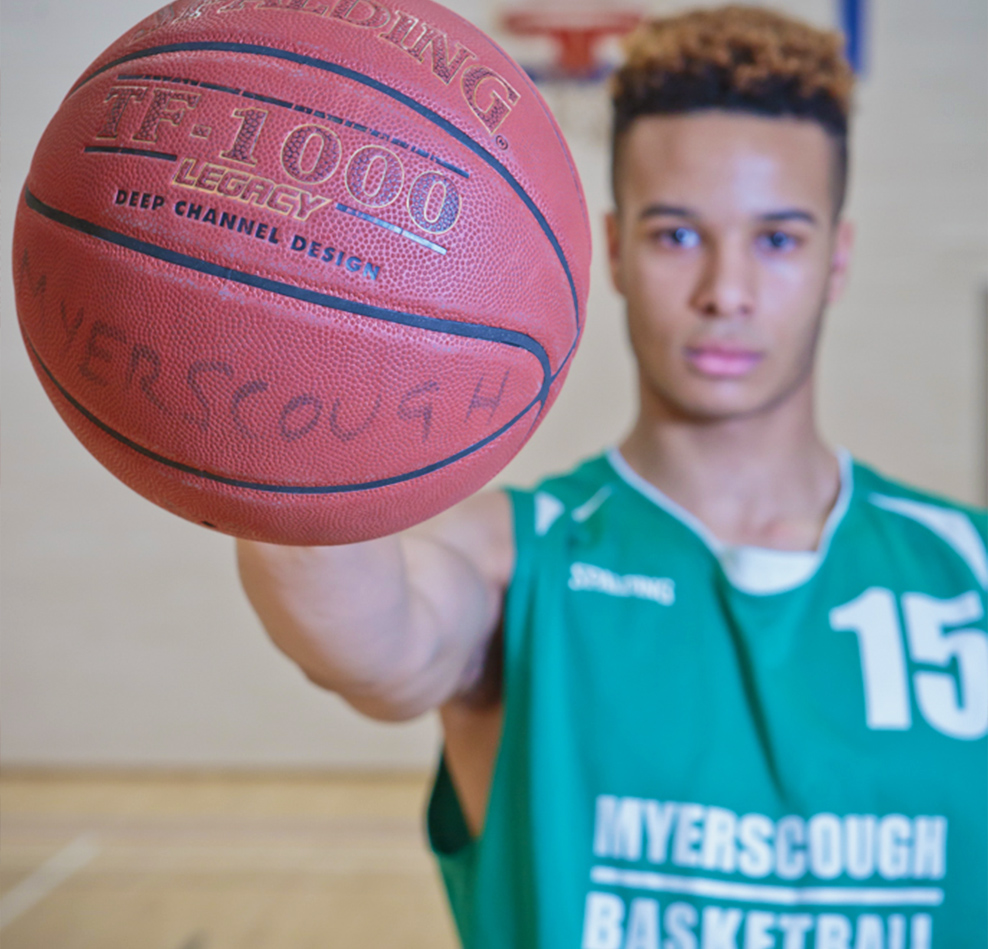 Myerscough College student holds up a basketball in a basketball court.